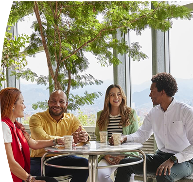 Cuatro personas conversan y disfrutan de un café en terraza con plantas y vista panorámica de la ciudad y montañas