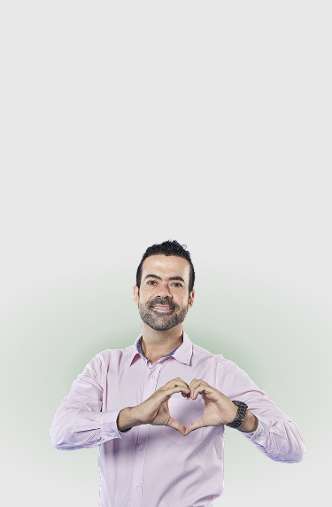 Hombre con camisa lila sonriendo hace gesto de corazón con las manos, sobre fondo claro
