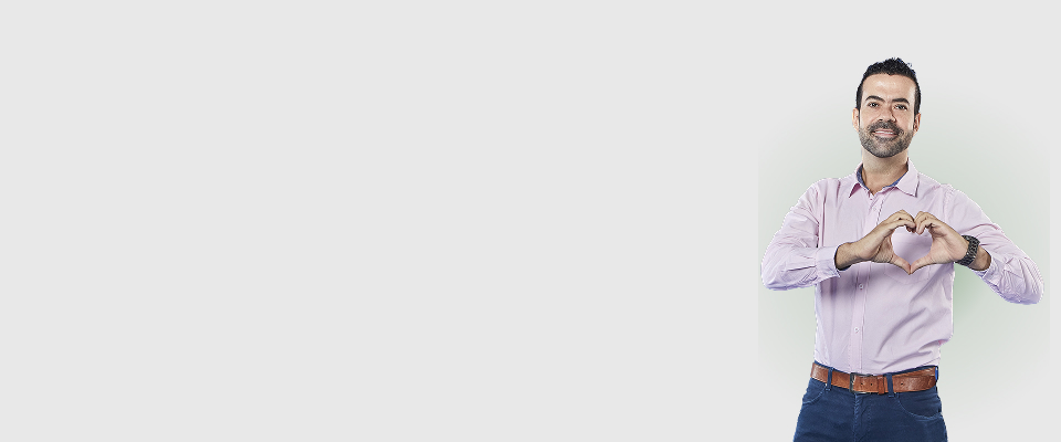 Hombre con camisa lila sonriendo hace gesto de corazón con las manos, sobre fondo claro