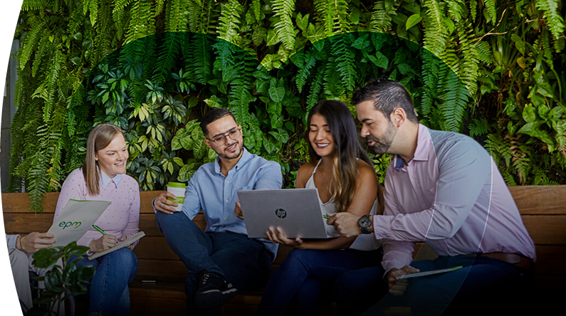 Empleados de EPM colaborando en equipo con laptops y documentos en un espacio verde sostenible con pared de plantas naturales