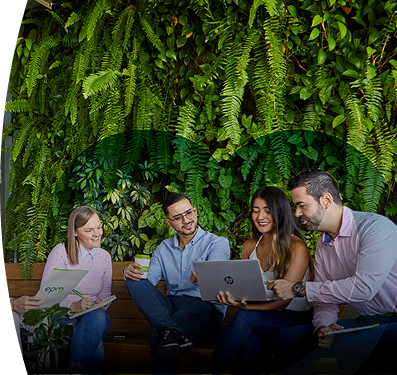 Empleados de EPM colaborando en equipo con laptops y documentos en un espacio verde sostenible con pared de plantas naturales