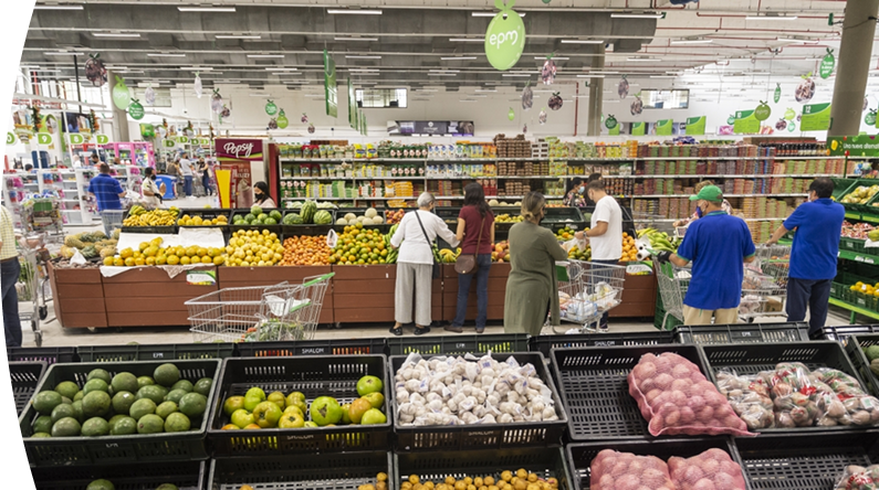Personas comprando frutas y verduras en supermercado con señalética de EPM