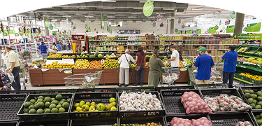 Personas comprando frutas y verduras en supermercado con señalética de EPM