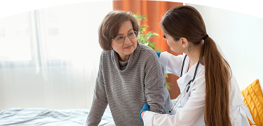 Doctora apoya a una mujer mayor que usa caminador, sosteniéndola del brazo