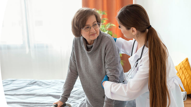 Doctora apoya a una mujer mayor que usa caminador, sosteniéndola del brazo