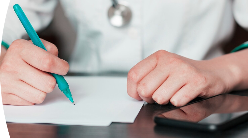 Persona escribiendo con un bolígrafo sobre una hoja de papel, con un teléfono móvil negro sobre la mesa.