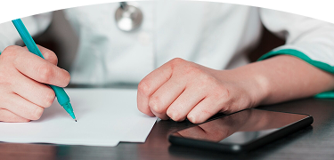 Persona escribiendo con un bolígrafo sobre una hoja de papel, con un teléfono móvil negro sobre la mesa.