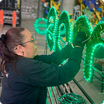 Mujer de camisa negra y guantes instalando luces en figuras navideñas de los alumbrados EPM