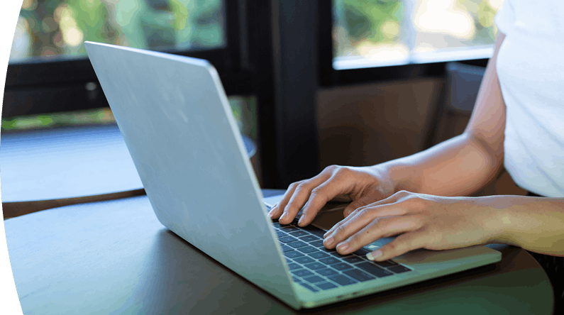 Persona escribiendo en el teclado de una computadora portátil sobre una mesa de madera