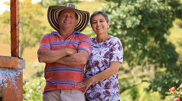 Pareja campesina sonríe frente a su hogar con el mensaje “Juntos por el desarrollo de la región”, en un entorno rural