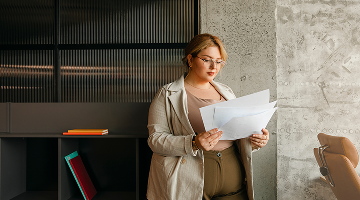 Mujer profesional revisando documentos en una oficina moderna con paredes de concreto y mobiliario corporativo