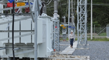 Ingeniera recorriendo subestación eléctrica con transformadores y torres metálicas