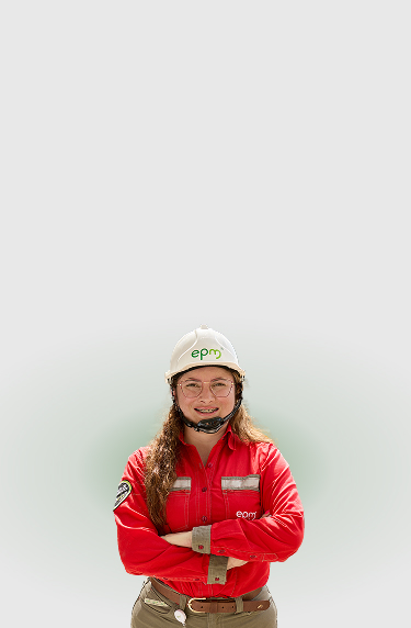 Colaboradora de EPM con uniforme rojo y casco de seguridad, sonríe con los brazos cruzados sobre fondo claro.
