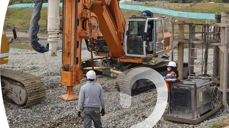 Banner ''Proyectos en el territorio'' obreros con casco de seguridad supervisando maquinaria pesada en una obra de construcción sobre terreno de grava, con excavadora hidráulica y equipo de perforación en funcionamiento