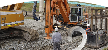 Banner ''Proyectos en el territorio'' obreros con casco de seguridad supervisando maquinaria pesada en una obra de construcción sobre terreno de grava, con excavadora hidráulica y equipo de perforación en funcionamiento