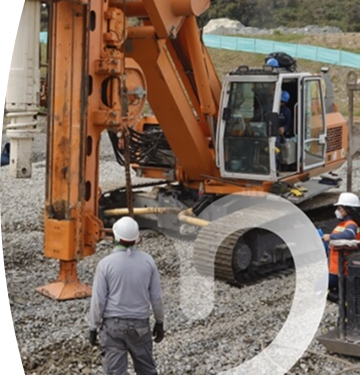 Banner ''Proyectos en el territorio'' obreros con casco de seguridad supervisando maquinaria pesada en una obra de construcción sobre terreno de grava, con excavadora hidráulica y equipo de perforación en funcionamiento