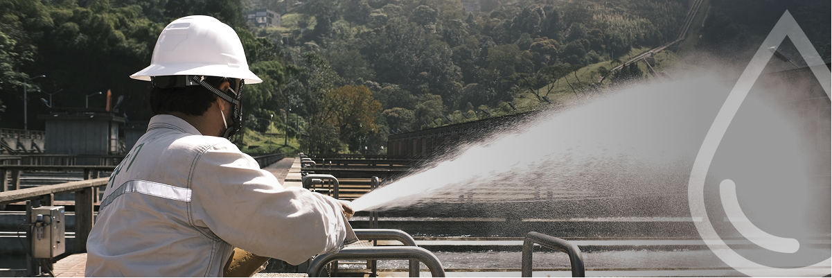 Empelado de EPM regando agua con manguera a presión. Al fondo se observan árboles