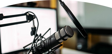 Primer plano de un micrófono de estudio profesional frente a una pantalla de computadora en un entorno de grabación o podcast.