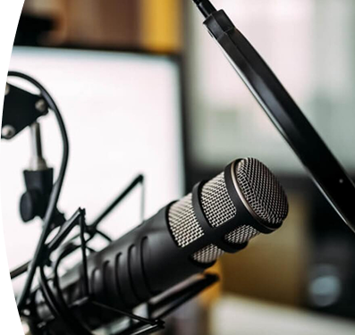 Primer plano de un micrófono de estudio profesional frente a una pantalla de computadora en un entorno de grabación o podcast.