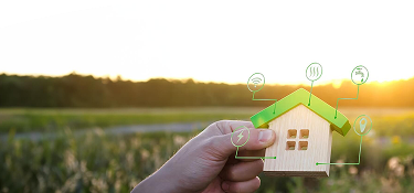 Mano sosteniendo una casa de madera en miniatura con íconos que representan servicios como electricidad, agua, gas, internet e iluminación