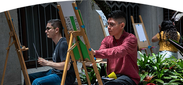 Personas realizando actividades de pintura artística en caballetes durante una jornada cultural.