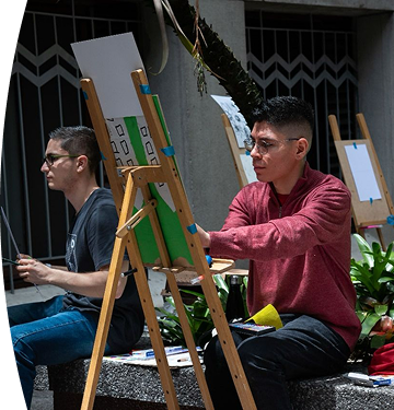Personas realizando actividades de pintura artística en caballetes durante una jornada cultural.