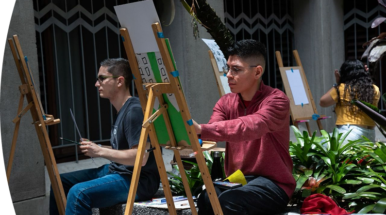 Personas realizando actividades de pintura artística en caballetes durante una jornada cultural.