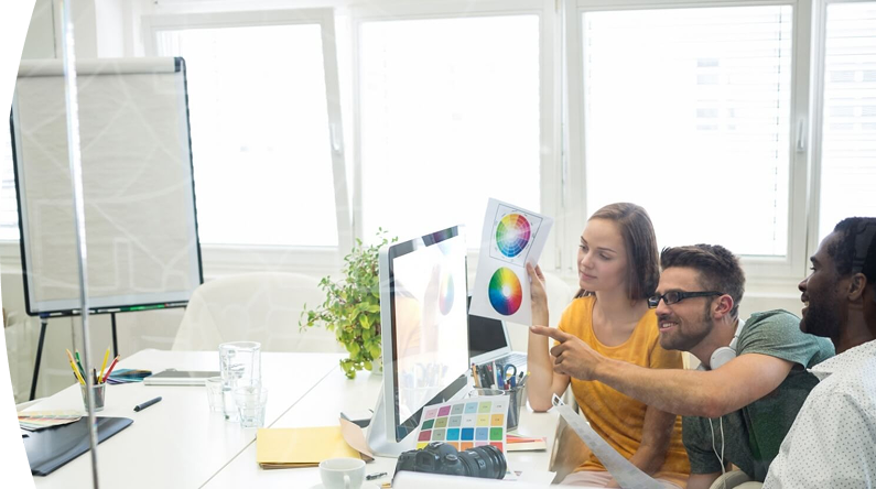 Equipo creativo revisando paletas de colores frente a una computadora, en una reunión de diseño publicitario en oficina moderna.