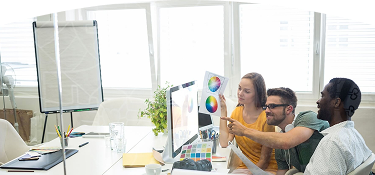 Equipo creativo revisando paletas de colores frente a una computadora, en una reunión de diseño publicitario en oficina moderna.