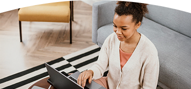 Persona sentada en una sala de estar trabajando en un computador portátil sobre una mesa baja