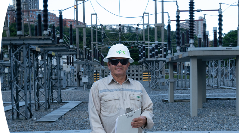 Trabajador de EPM parado en una planta eléctrica con un portapapeles en la mano