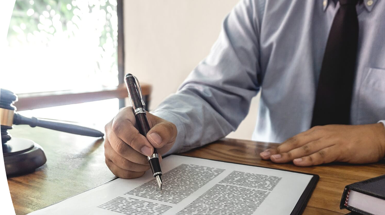 Abogado con camisa azul y corbata negra revisando y firmando documento legal en escritorio con mazo judicial