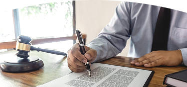 Abogado con camisa azul y corbata negra revisando y firmando documento legal en escritorio con mazo judicial