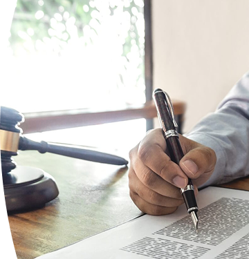 Abogado con camisa azul y corbata negra revisando y firmando documento legal en escritorio con mazo judicial