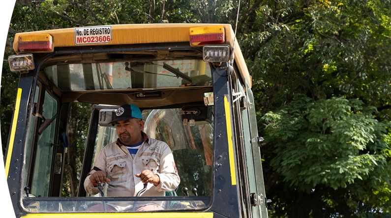 Operario de EPM maneja maquinaria pesada en campo, usando uniforme y gorra, en labores de mantenimiento de infraestructura pública