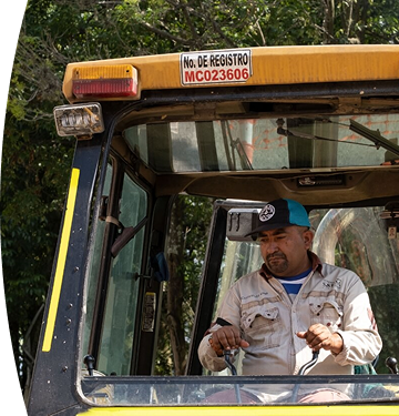 Operario de EPM maneja maquinaria pesada en campo, usando uniforme y gorra, en labores de mantenimiento de infraestructura pública