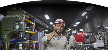 Trabajador sonriente con casco dando un pulgar arriba en un entorno industrial.