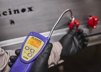 Técnico con guantes negros utilizando detector de fugas de gas frente a válvula industrial