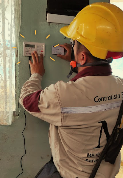 Fotografía de un trabajador con casco amarillo y uniforme de contratista instala o revisa un medidor de energía prepago en una pared interior