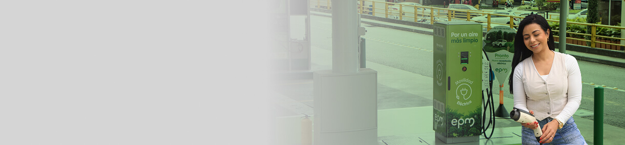 Mujer sonriente de pie junto a una estación de recarga de vehículos eléctricos de EPM
