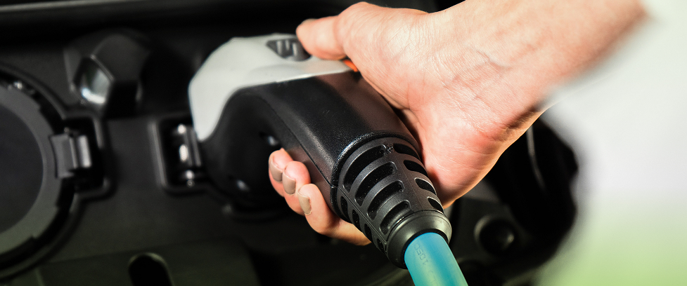 Primer plano de una mano conectando un cargador de energía al puerto de un vehículo eléctrico