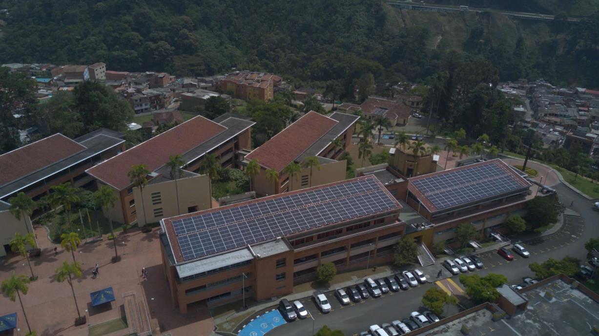 Vista aérea de un complejo institucional en medio de zona montañosa, con edificios de techos rojos equipados con paneles solares fotovoltaicos y parqueadero con varios vehículos