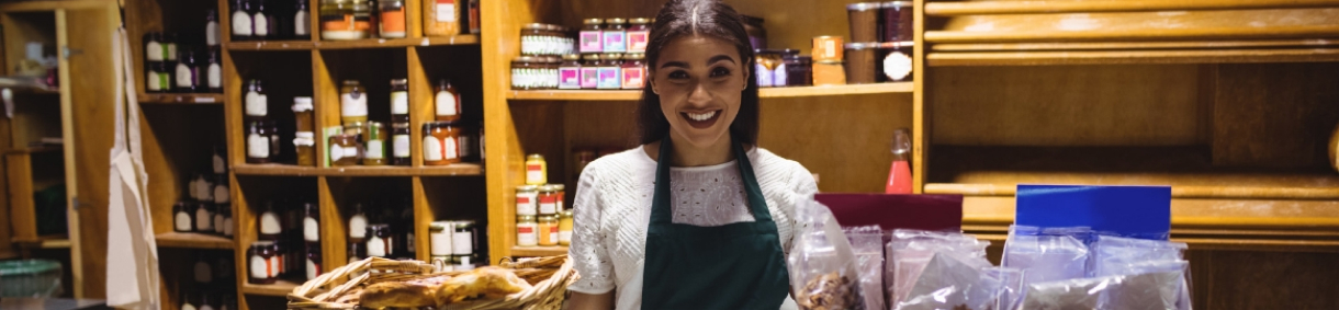 Mujer sonriente atendiendo en un negocio o tienda con estantes de productos en el fondo
