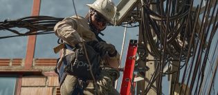 Técnico electricista de EPM realiza trabajos en redes eléctricas utilizando equipo de protección y herramientas especializadas.