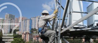 Un trabajador de mantenimiento se encuentra subiendo por una torre de telecomunicaciones, equipado con un arnés de seguridad y casco