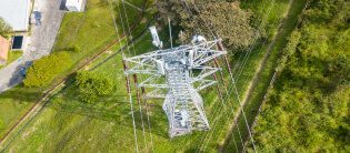 Vista aérea de una torre de transmisión eléctrica ubicada en un área verde, con líneas de transmisión que se extienden hacia diferentes direcciones.