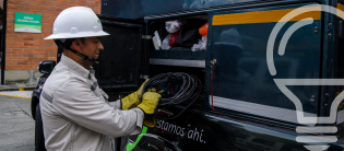 Técnico EPM con casco y guantes sacando cable de vehículo de servicio, ícono de bombilla de fondo
