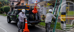 Tres trabajadores EPM con equipo de seguridad colocan conos y una escalera para labores de mantenimiento urbano