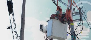 Trabajador en una plataforma elevadora realizando mantenimiento en una torre de cables eléctricos al aire libre