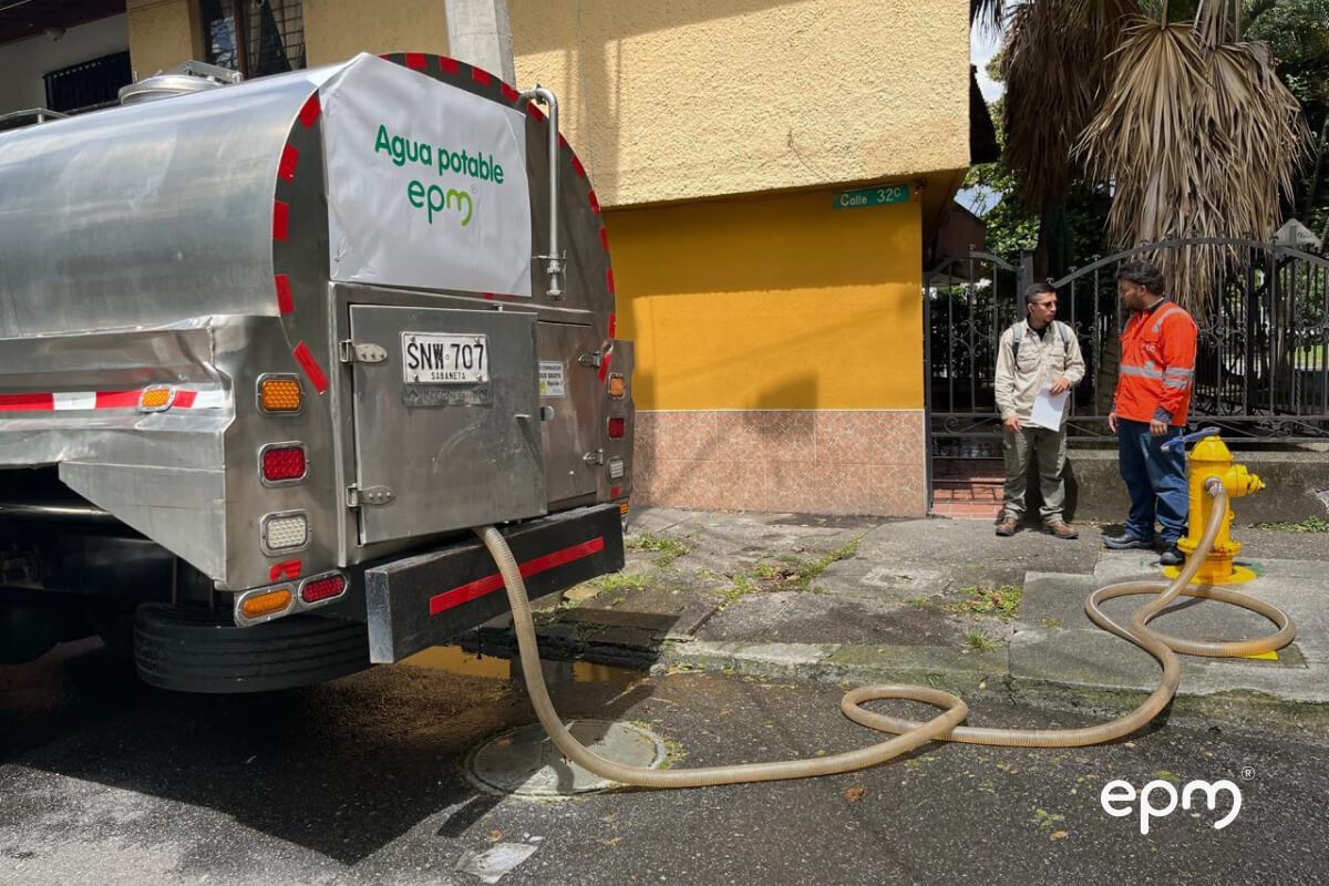 Fotografía de un camión de EPM suministrando agua potable a través de una manguera conectada a un hidrante, en zona urbana